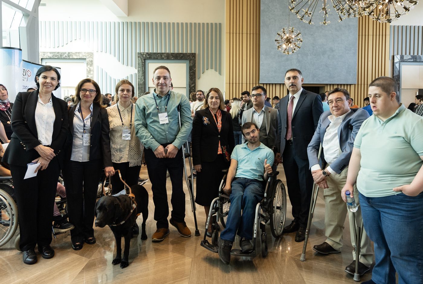 A large group photograph in a bright atrium. The people include wheelchair users, crutch users and a guide dog with its handler.